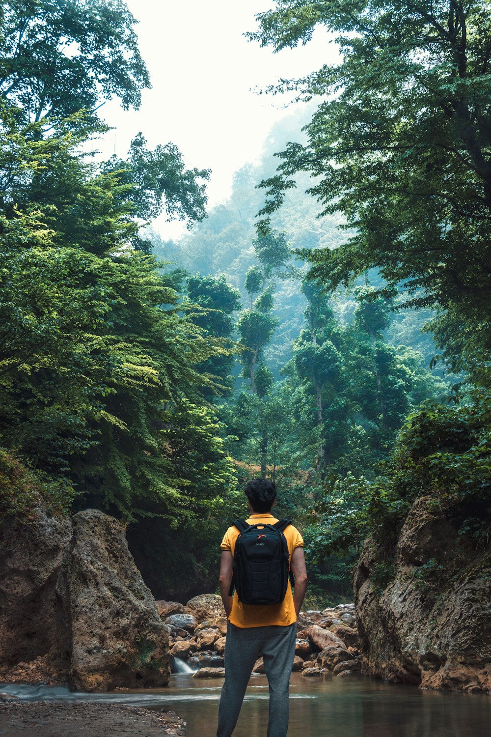 man in yellow tank top and black shorts standing on rocky hill during daytime