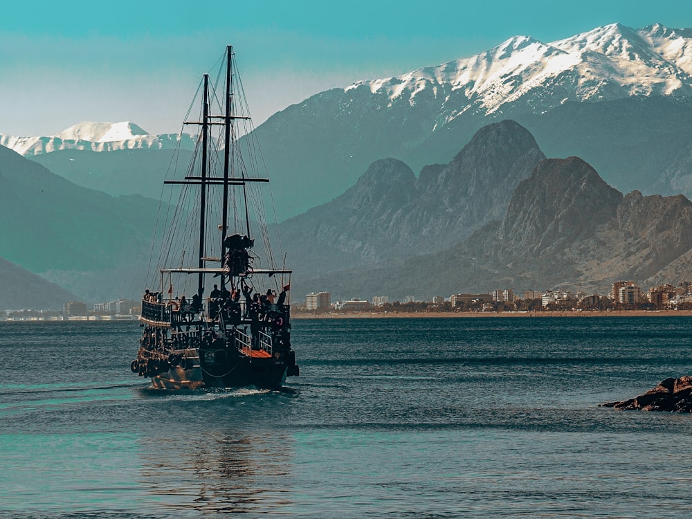 black sail boat on sea near snow covered mountain during daytime