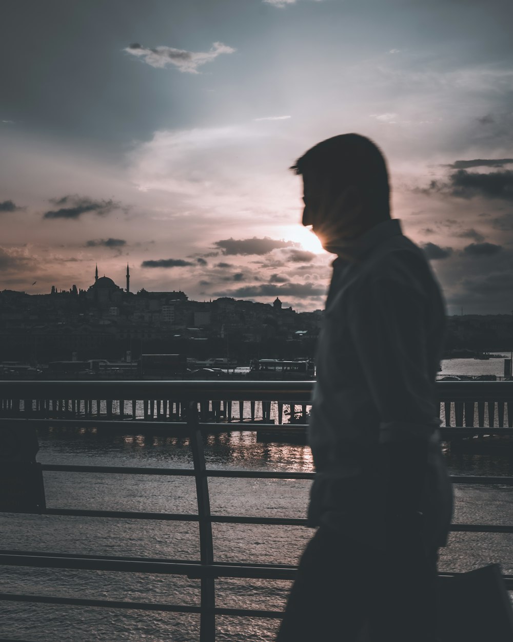 silhouette of man standing near body of water during sunset