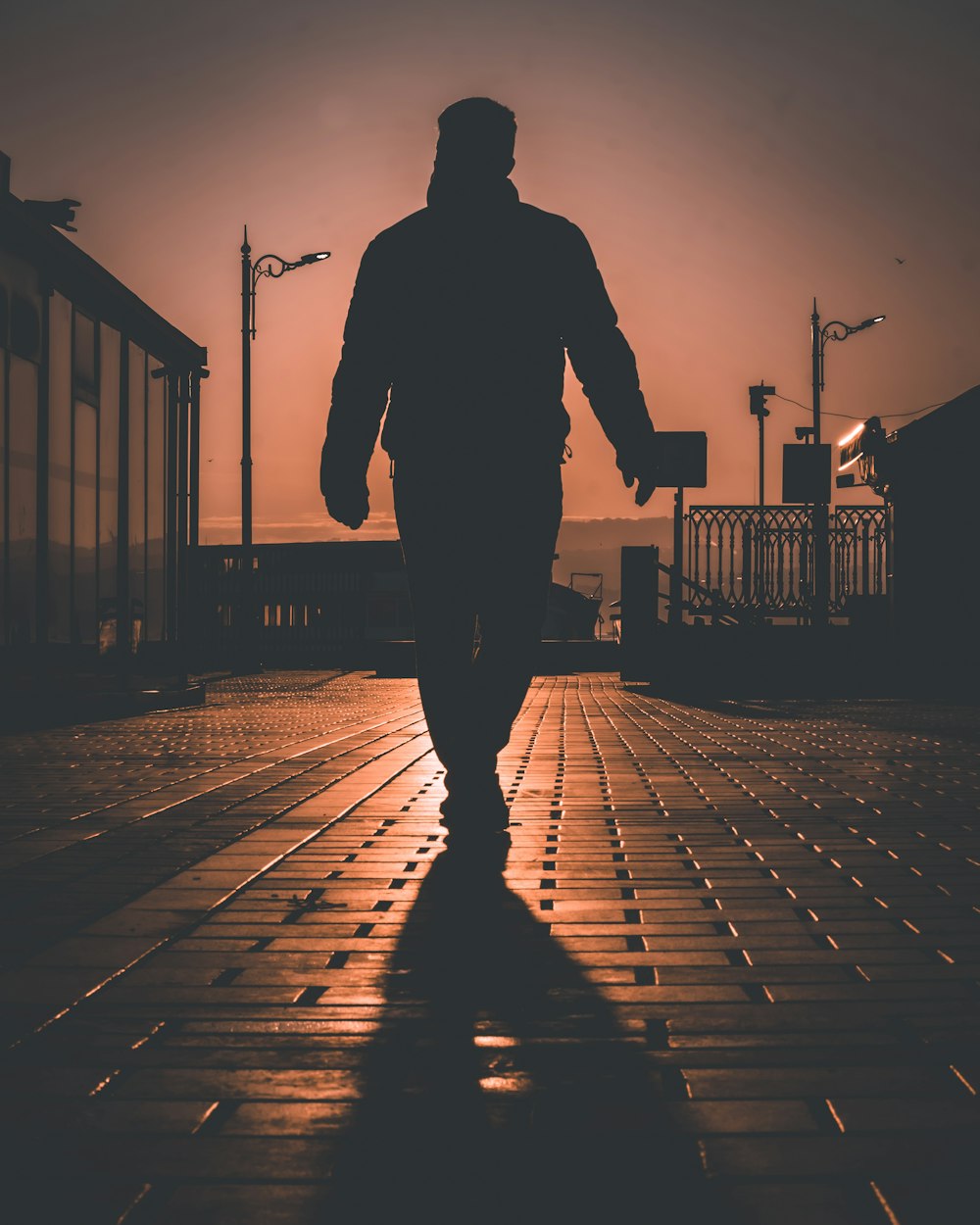 silhouette of man walking on sidewalk during sunset