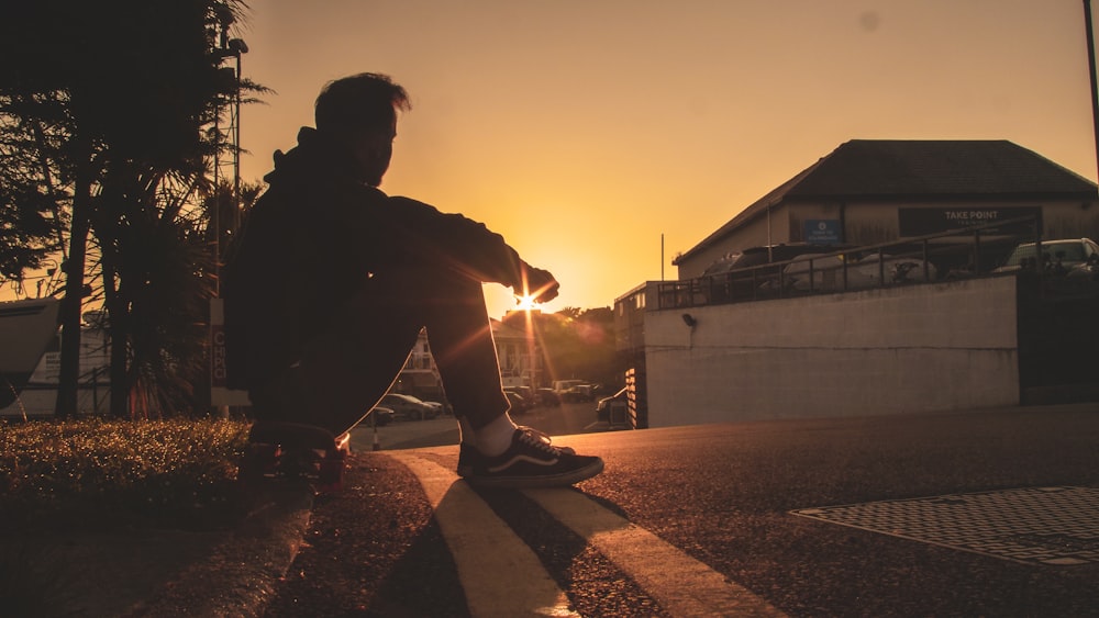 man in black jacket and pants sitting on concrete wall during sunset