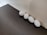 Four white eggs are arranged in a straight line against a light-colored wall. The eggs rest on a dark wooden surface, creating a contrast between the white of the eggs and the dark texture of the table. The lighting is soft, casting gentle shadows around the eggs.