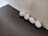 Four white eggs are arranged in a straight line against a light-colored wall. The eggs rest on a dark wooden surface, creating a contrast between the white of the eggs and the dark texture of the table. The lighting is soft, casting gentle shadows around the eggs.