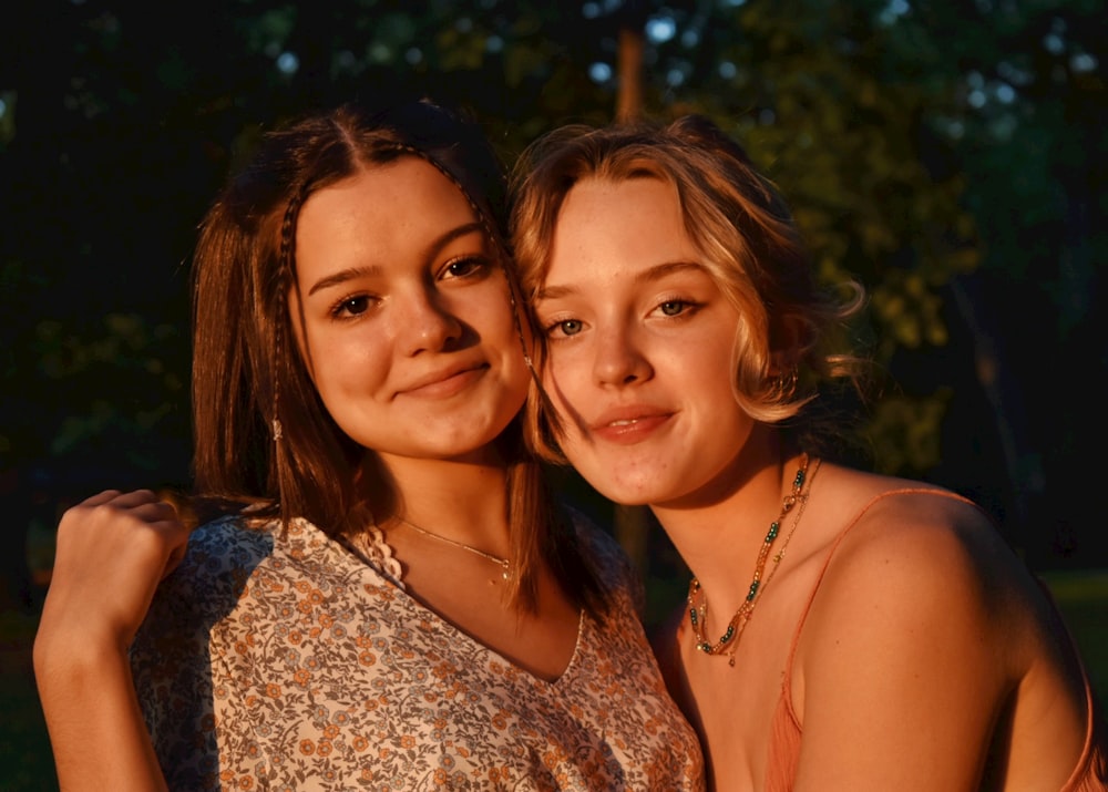 2 women smiling in front of green trees during daytime