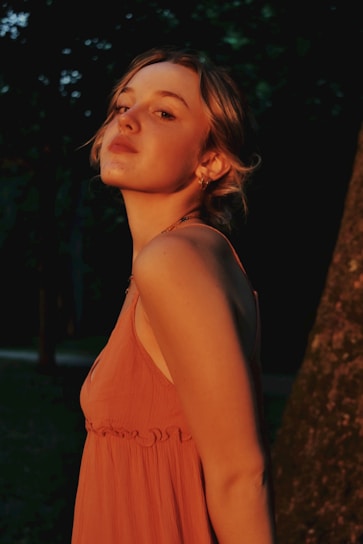 An editorial-style fashion image featuring a young woman illuminated by golden and pink lighting.