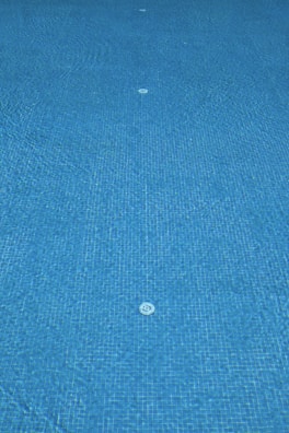 A view of a swimming pool floor covered in blue tiles with visible water drains placed in a symmetrical pattern.