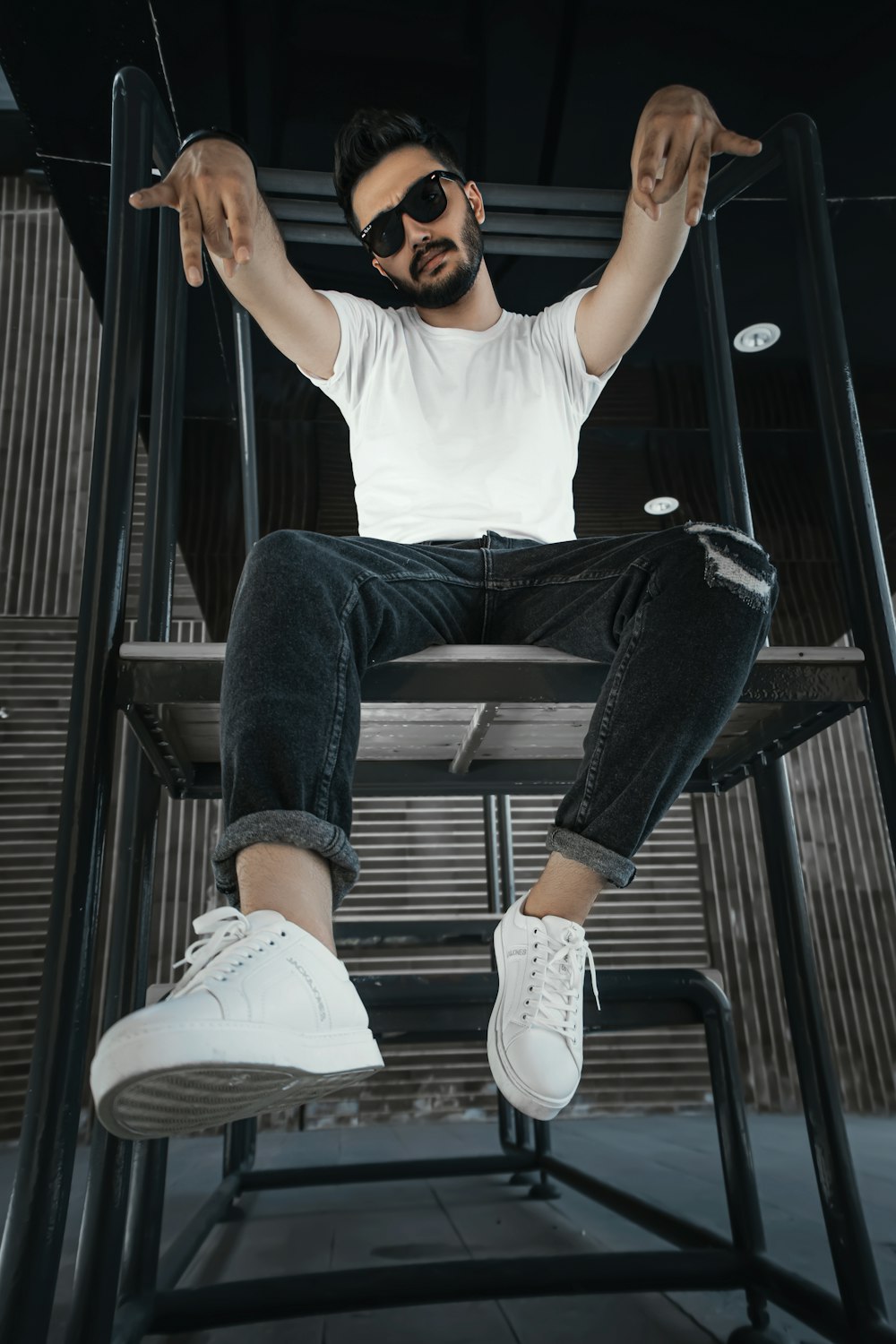 man in white t-shirt and black pants sitting on black metal stair