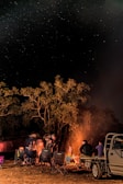A nighttime outdoor meetup with members sharing stories around a campfire under a starry sky.
