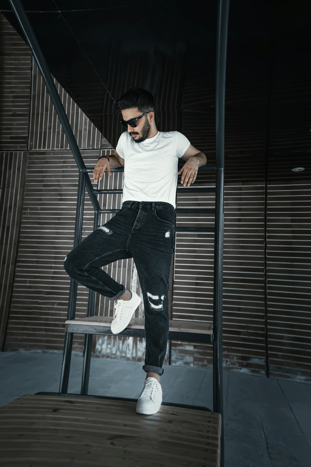 man in white t-shirt and blue denim jeans standing on black metal bar