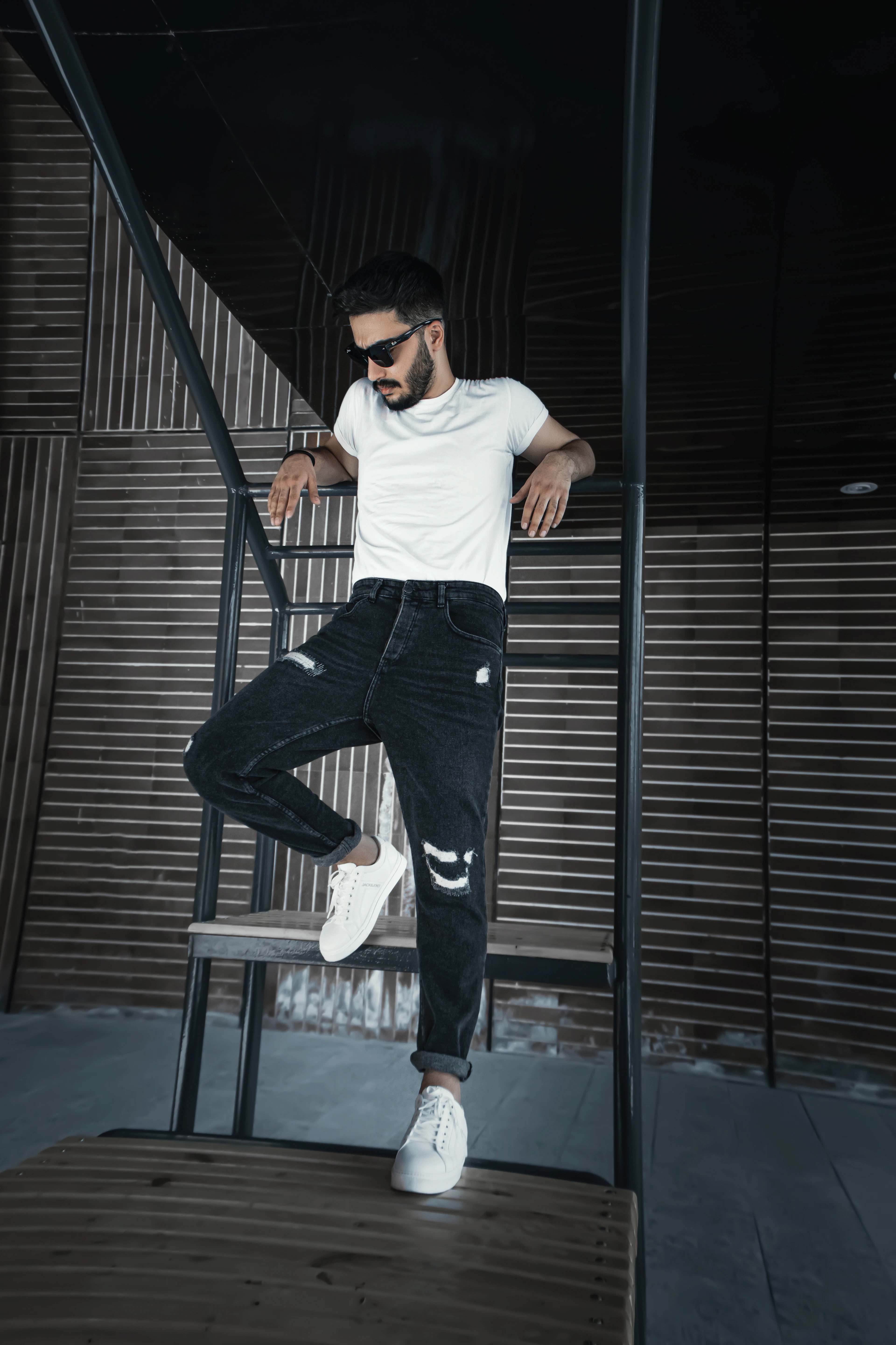 Man in a white tee and black ripped jeans perched on a metal rail