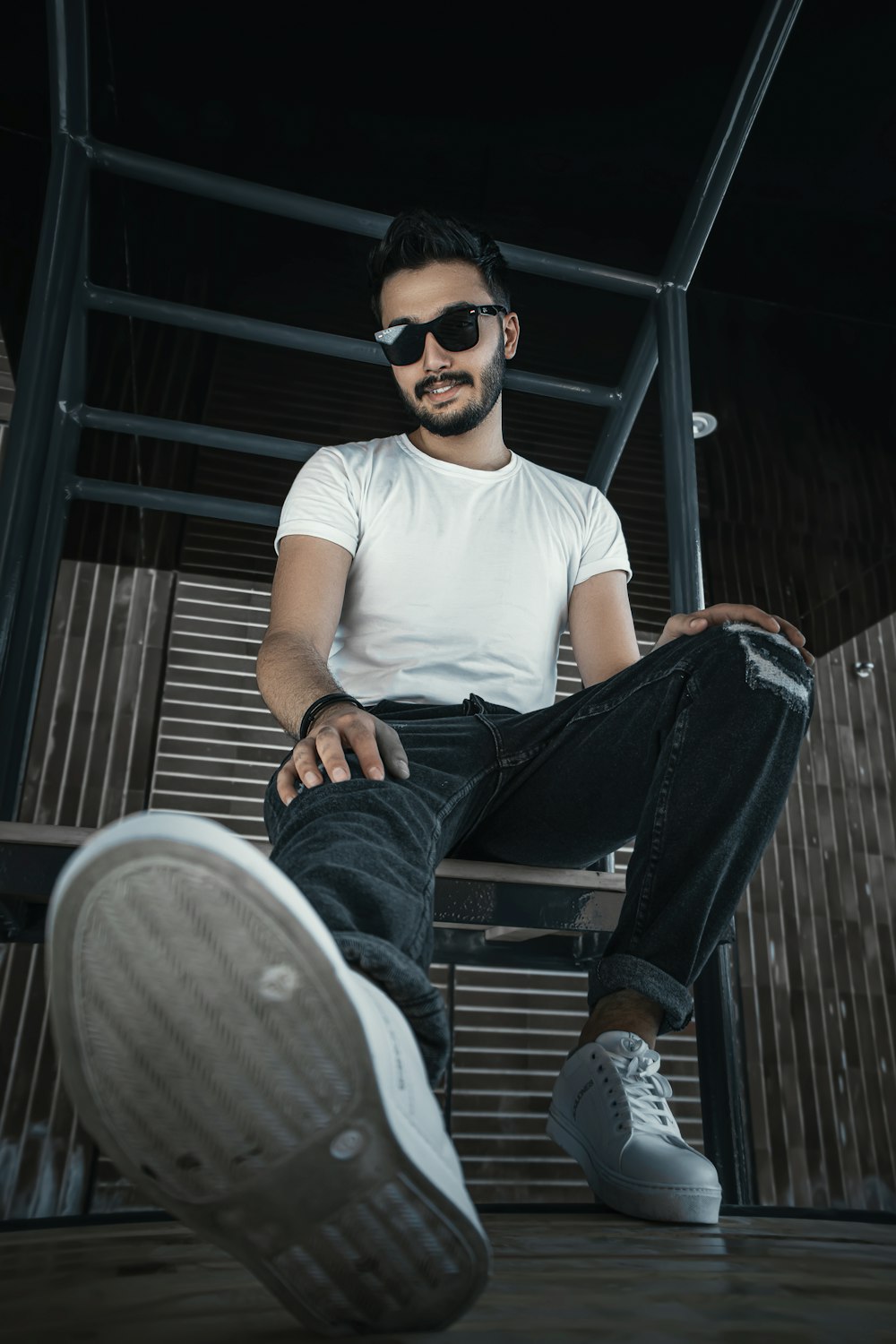 man in white crew neck t-shirt and blue denim jeans sitting on gray wooden bench