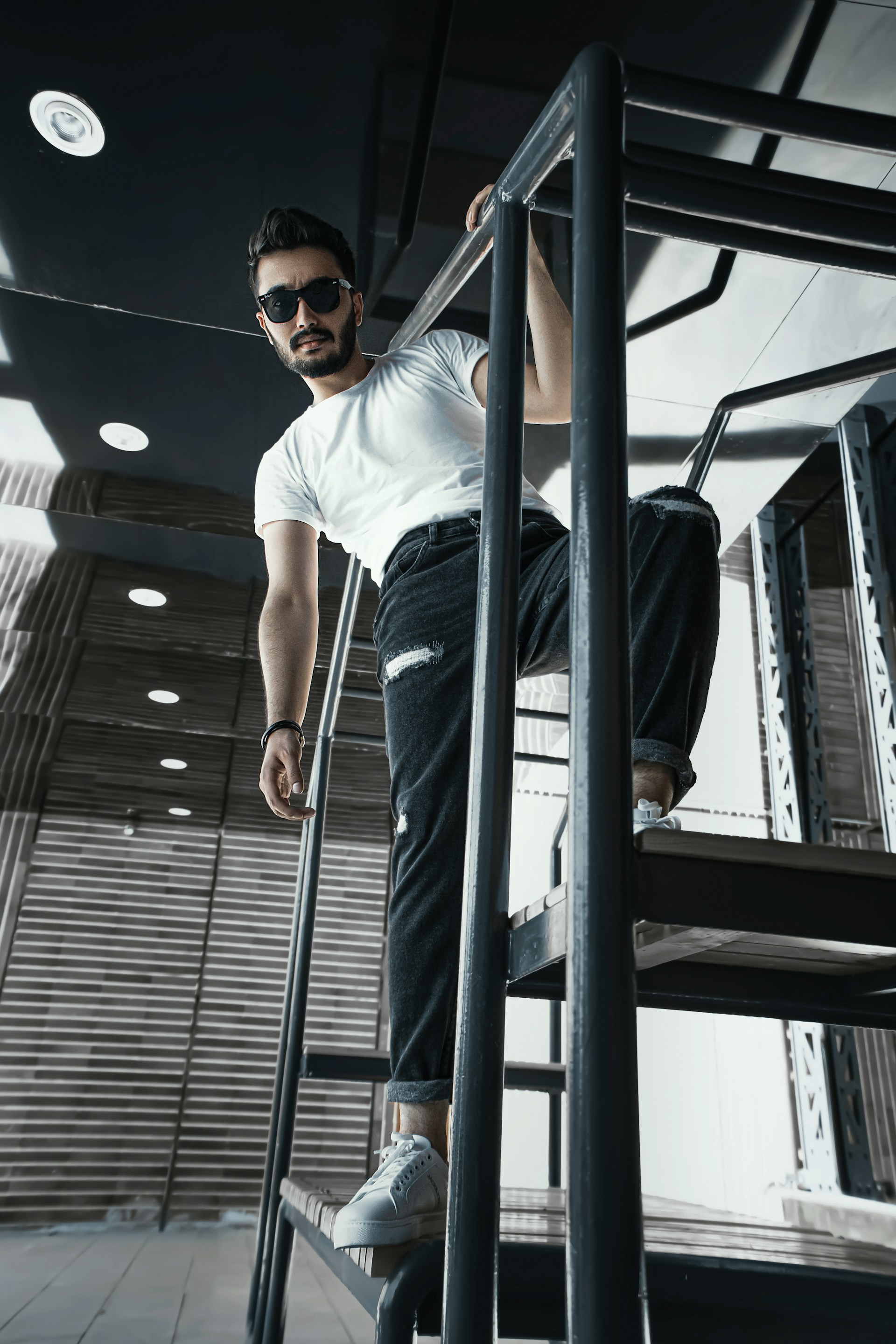 man in white crew neck t-shirt wearing black sunglasses standing beside gray metal railings