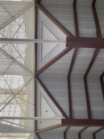 A geometric architectural design featuring triangular and rectangular patterns formed by metal beams and panels. The structures create a symmetrical and modern aesthetic with a combination of horizontal slats and angled beams.