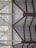 A geometric architectural design featuring triangular and rectangular patterns formed by metal beams and panels. The structures create a symmetrical and modern aesthetic with a combination of horizontal slats and angled beams.
