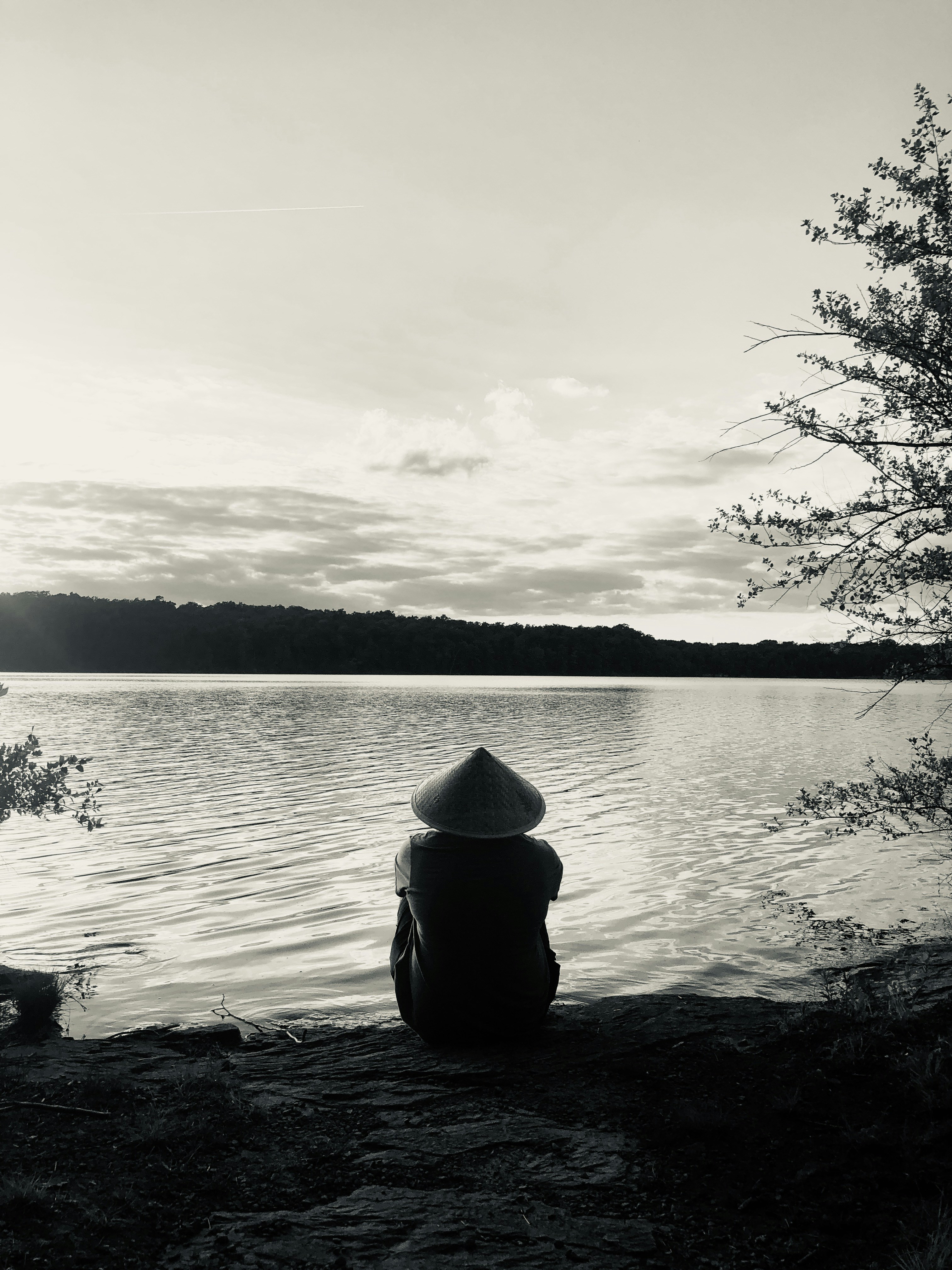 person in black hoodie sitting on rock near body of water during daytime