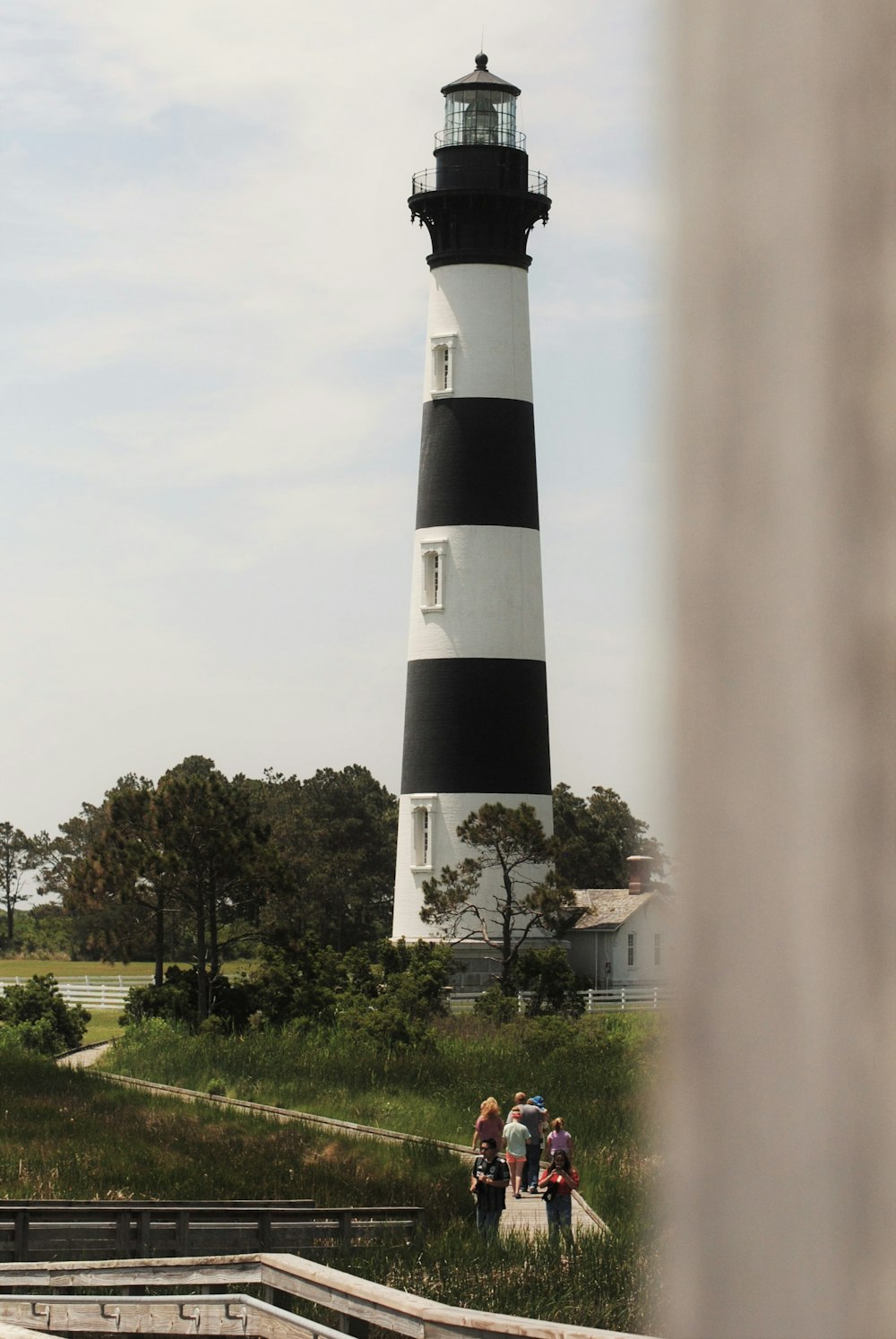 black and white lighthouse near green trees under white sky during daytime