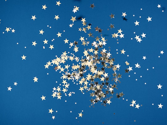 A scattering of golden star-shaped confetti is spread across a vibrant blue background, creating a playful and whimsical pattern.