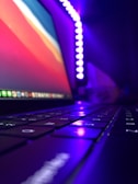 Close-up of hands coding on a laptop with vibrant purple and gold lighting.