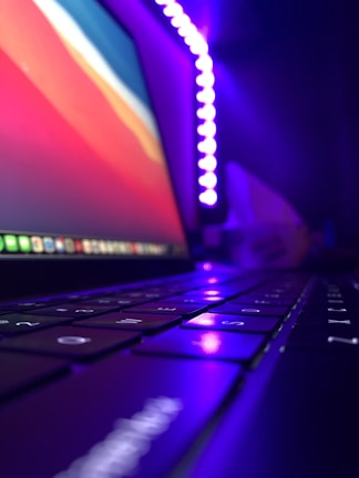 Close-up of hands coding on a laptop with vibrant purple and gold lighting.