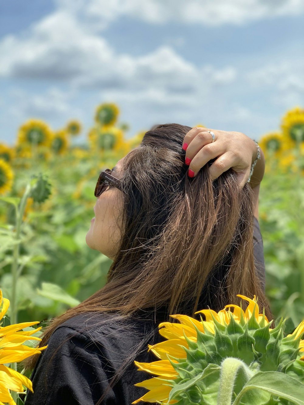 donna in camicia nera che copre il viso con i capelli sul campo di fiori gialli durante il giorno