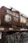 A rusted railway tanker, likely used for transporting flammable liquids, is situated on train tracks. The tanker is covered with graffiti and displays a sign indicating its maximum load capacity of 44,500 liters or 44.5 tonnes. There are steel ladders and walkways attached to the tanker, and dry vegetation can be seen in the foreground.