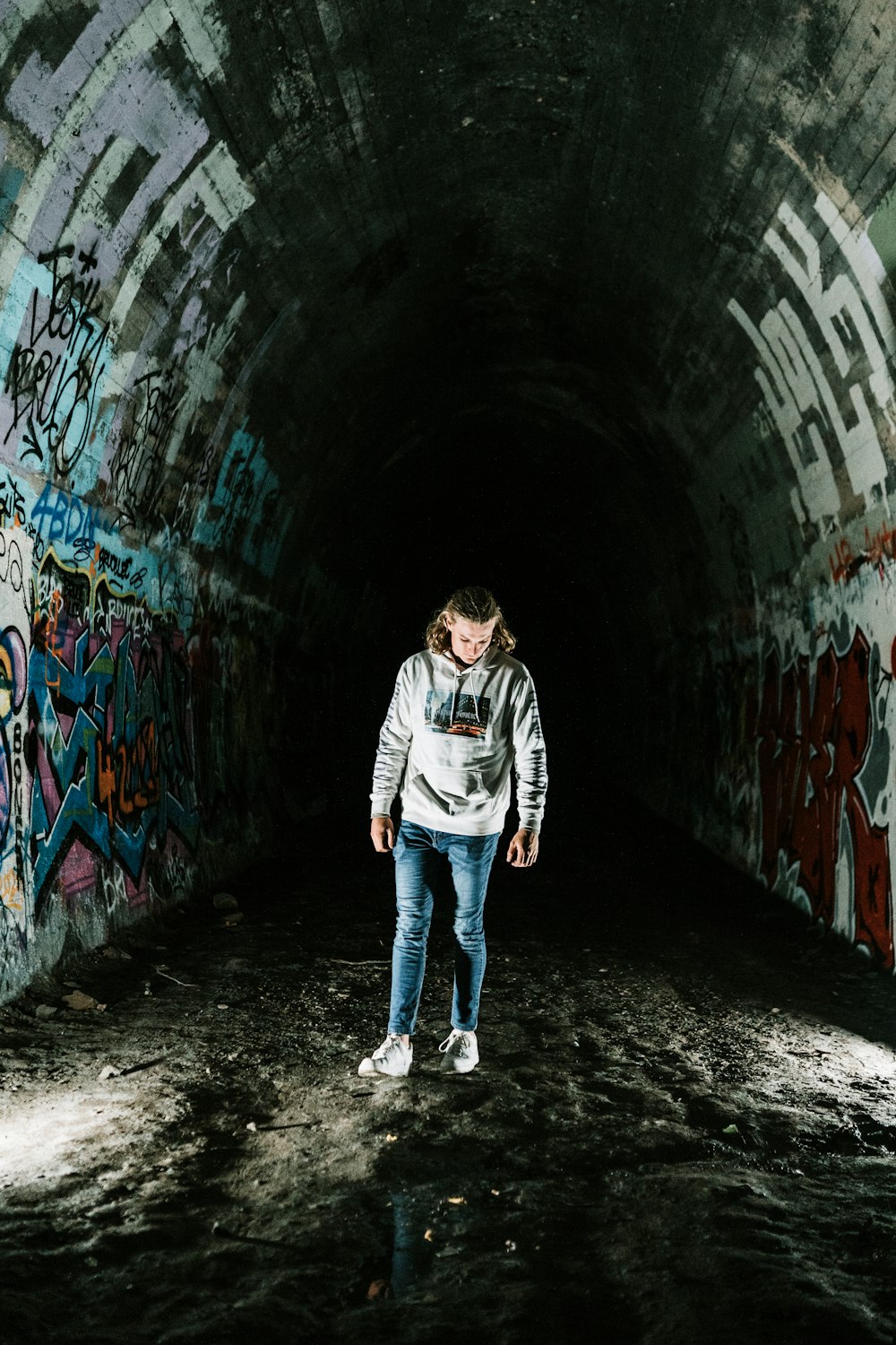 man in black and white jacket and blue denim jeans walking on tunnel