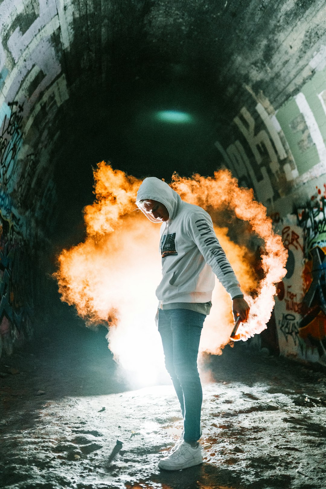 man in grey and black hoodie and blue denim jeans standing on tunnel with fire