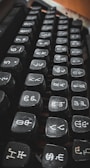 A close-up view of the keys on a typewriter, featuring unique symbols and numbers. The keys are black with white lettering, arranged in several rows and appearing slightly worn.