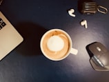 Bluetooth earphones resting beside a laptop and coffee cup.