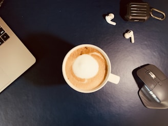 A set of stylish wireless headphones placed next to a laptop and a cup of coffee.