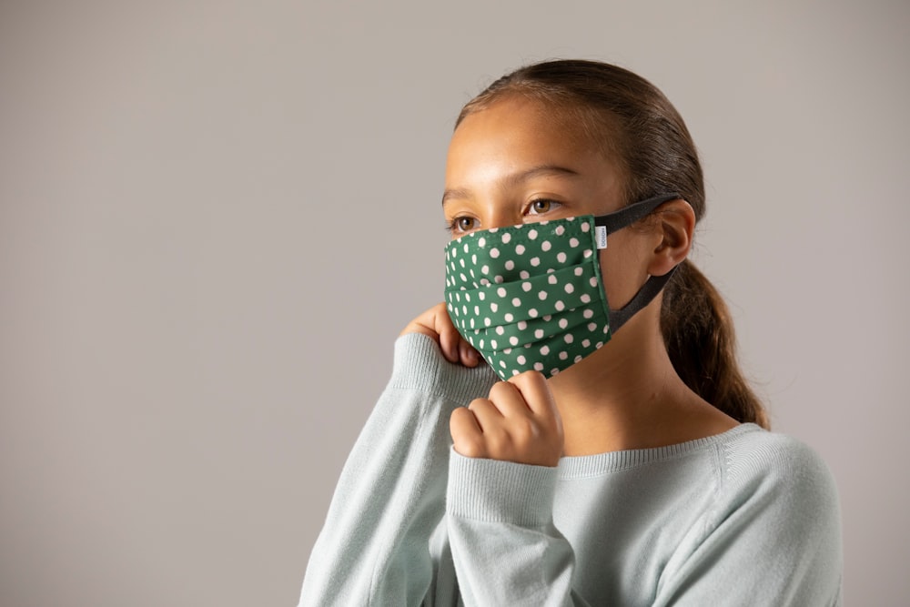 girl in teal sweater wearing black framed eyeglasses covering her face with green and white polka