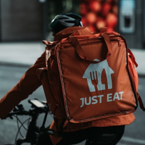 person in black jacket and orange and black backpack walking on sidewalk during daytime