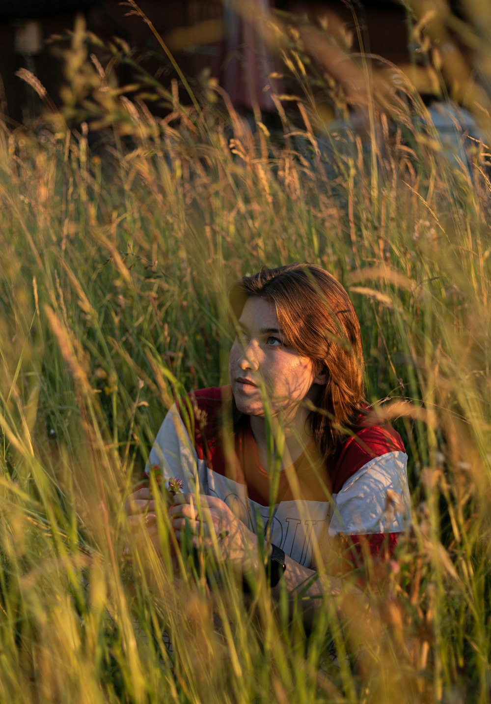 Femme en chemise rouge et blanche assise sur un champ d’herbe brune pendant la journée