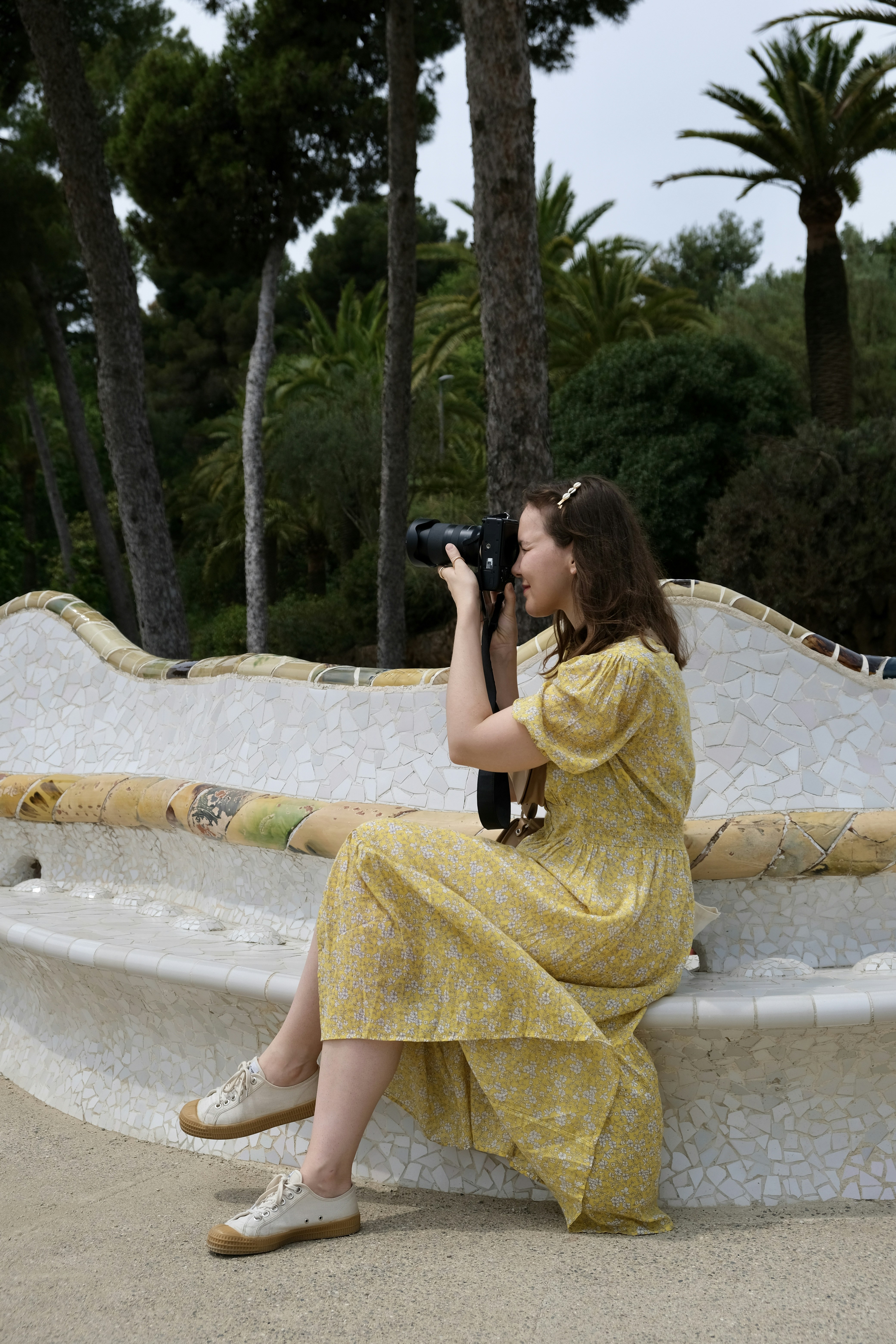 woman in yellow dress taking photo of green trees during daytime