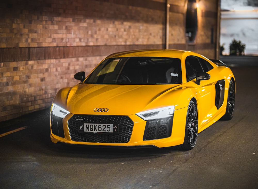 yellow porsche 911 parked beside brown brick wall