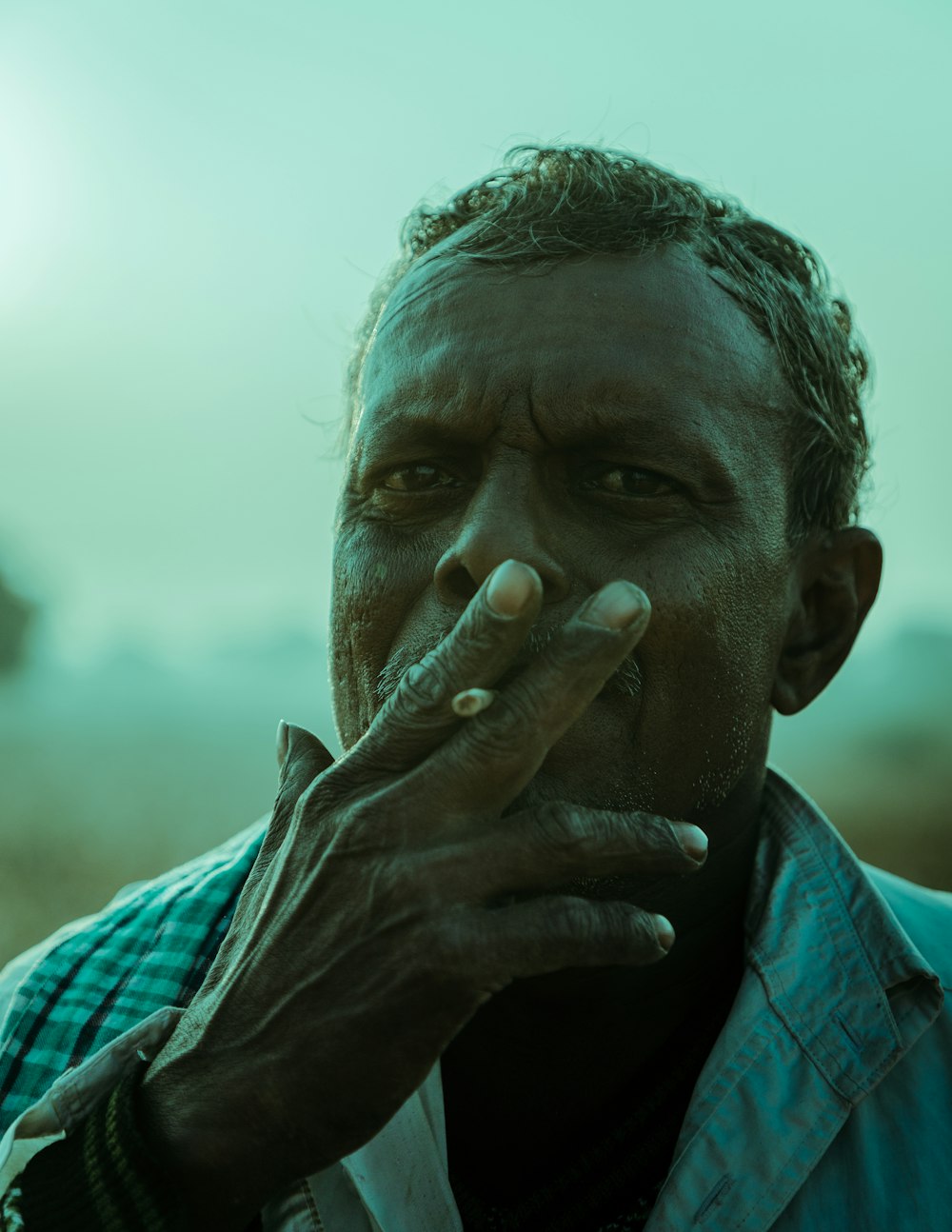 man in blue and white plaid shirt covering his face