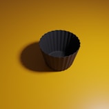 A dark, fluted cupcake mold is centered on a warm yellow background, casting a soft shadow to the left.