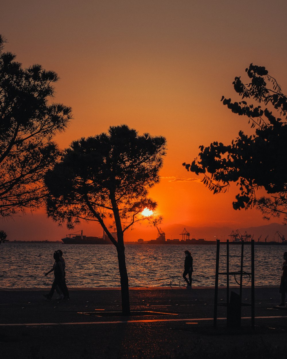 silhouette di persone in piedi vicino allo specchio d'acqua durante il tramonto