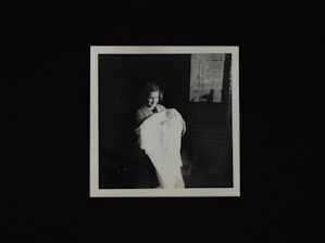 A smiling Indian mother gently holding her baby wrapped in a soft pastel blanket with fairy lights glowing softly in the background.