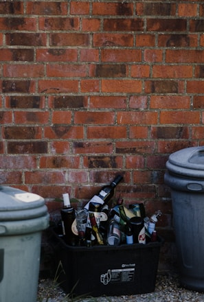 white plastic trash bin beside brown brick wall