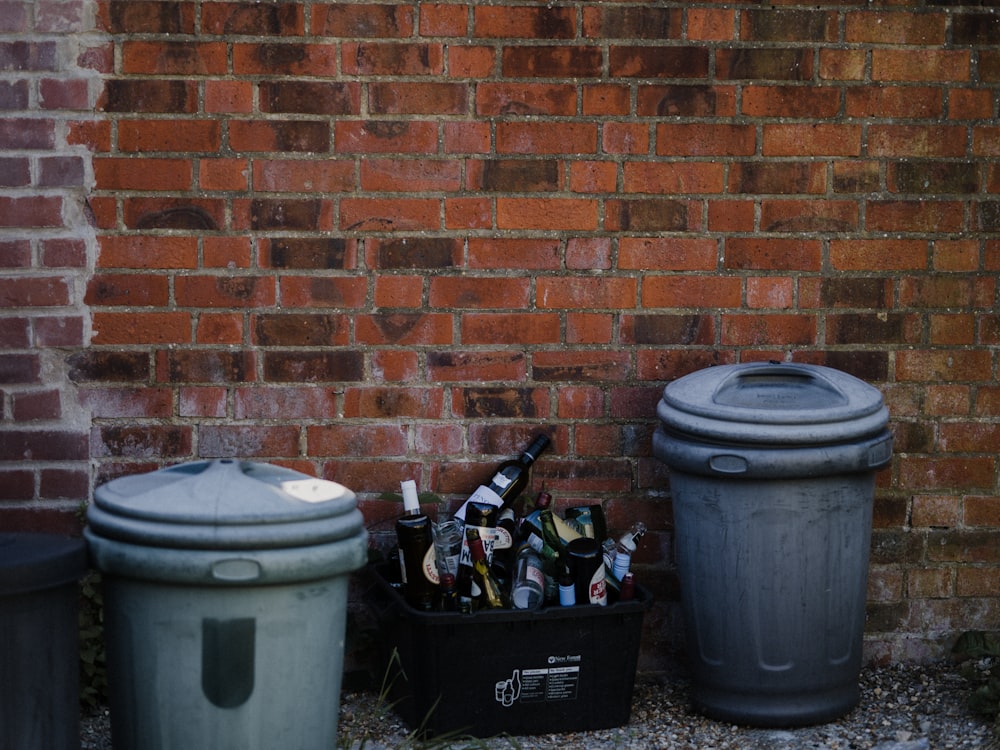 white plastic trash bin beside brown brick wall