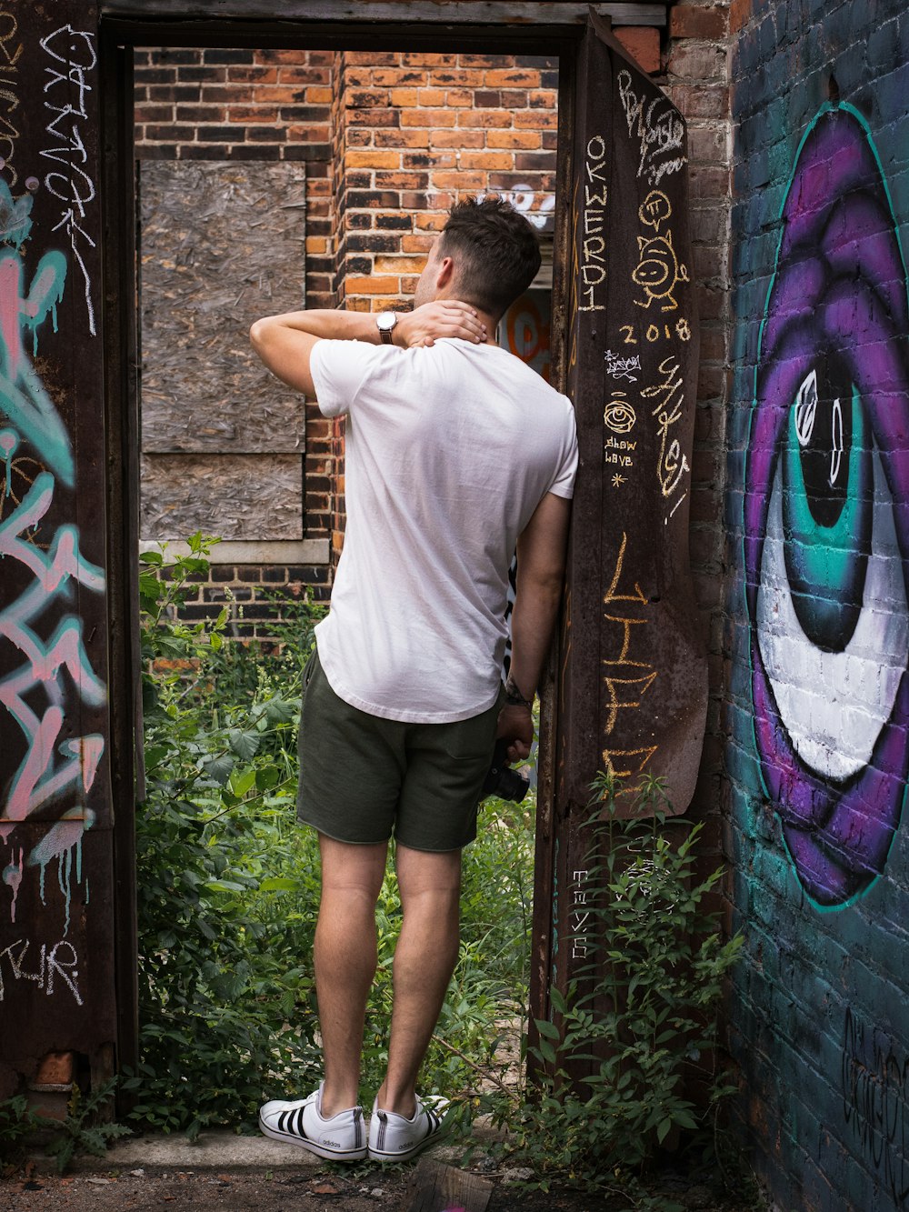 man in white t-shirt and black shorts standing beside brown wooden door