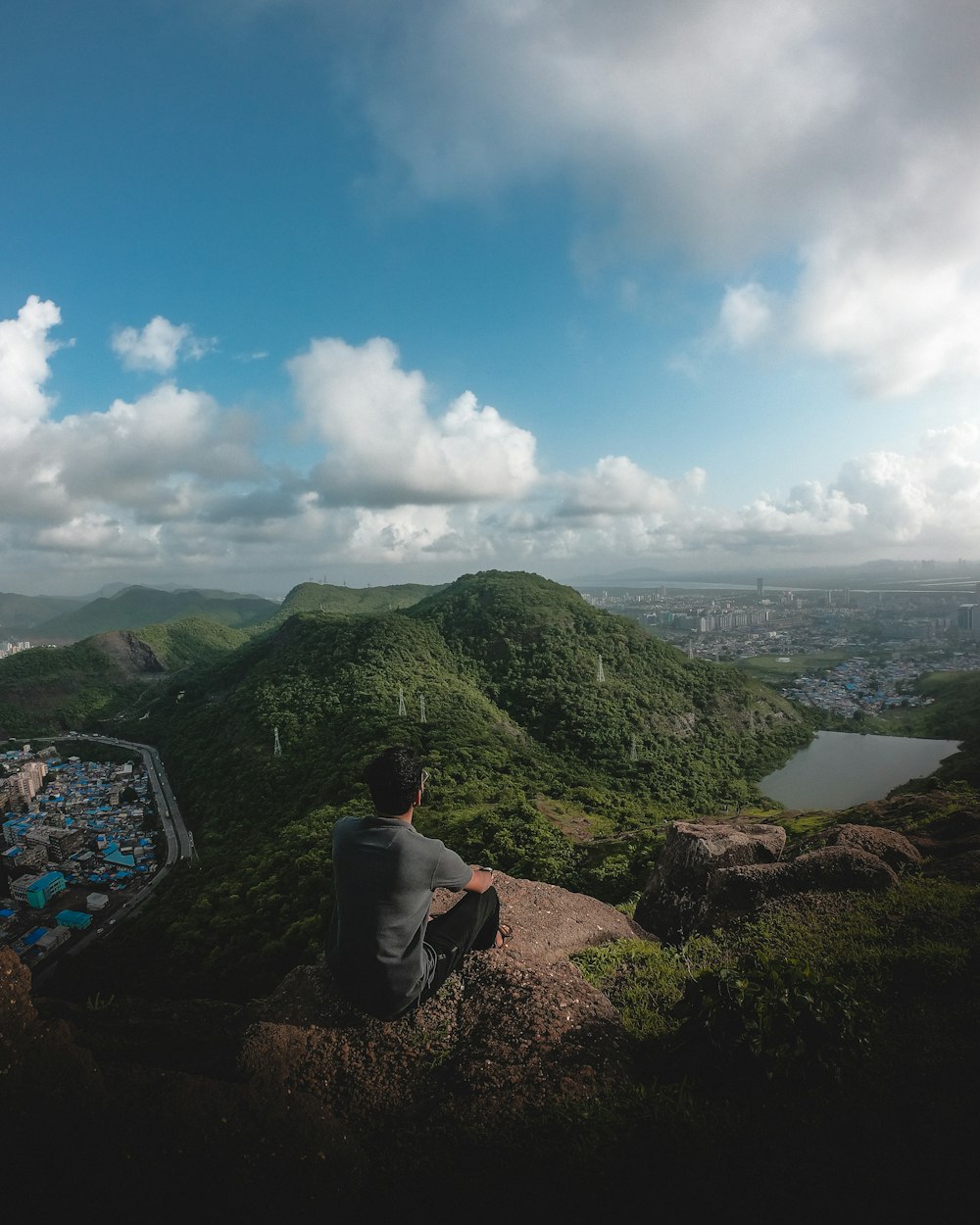 man in black shirt sitting on brown rock near green mountains during daytime