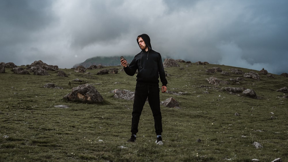 man in black jacket standing on green grass field under gray cloudy sky during daytime