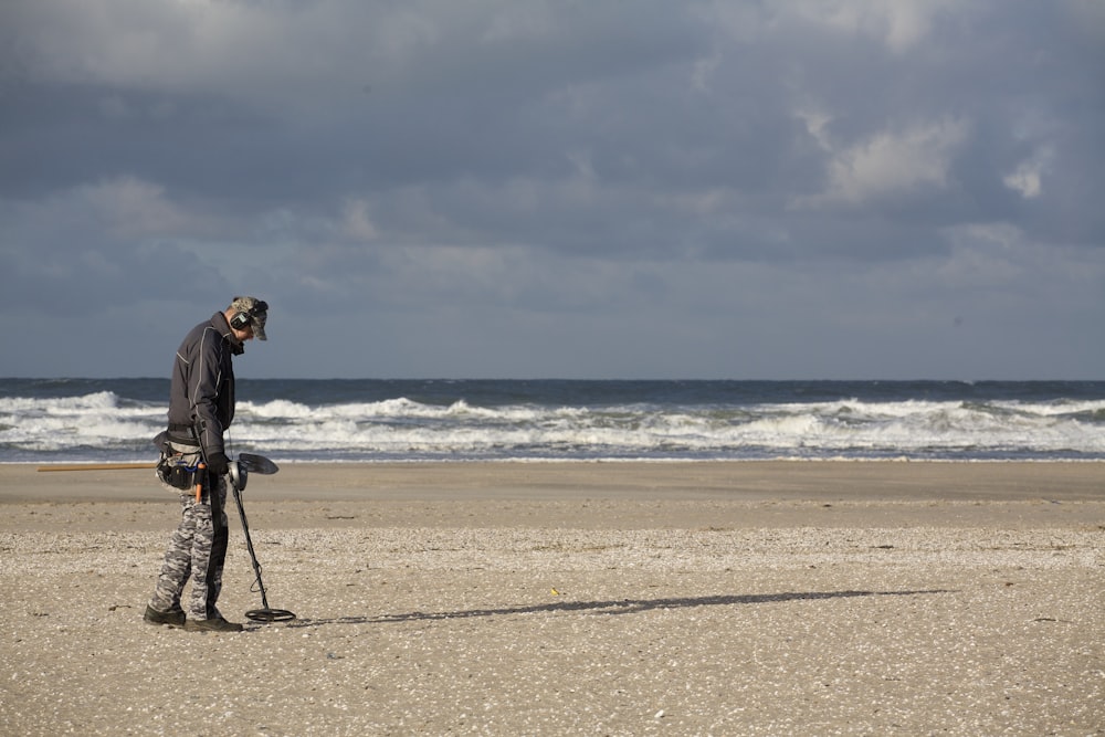 Mann in schwarzer Jacke und schwarzer Hose mit schwarzer DSLR-Kamera am Strand tagsüber