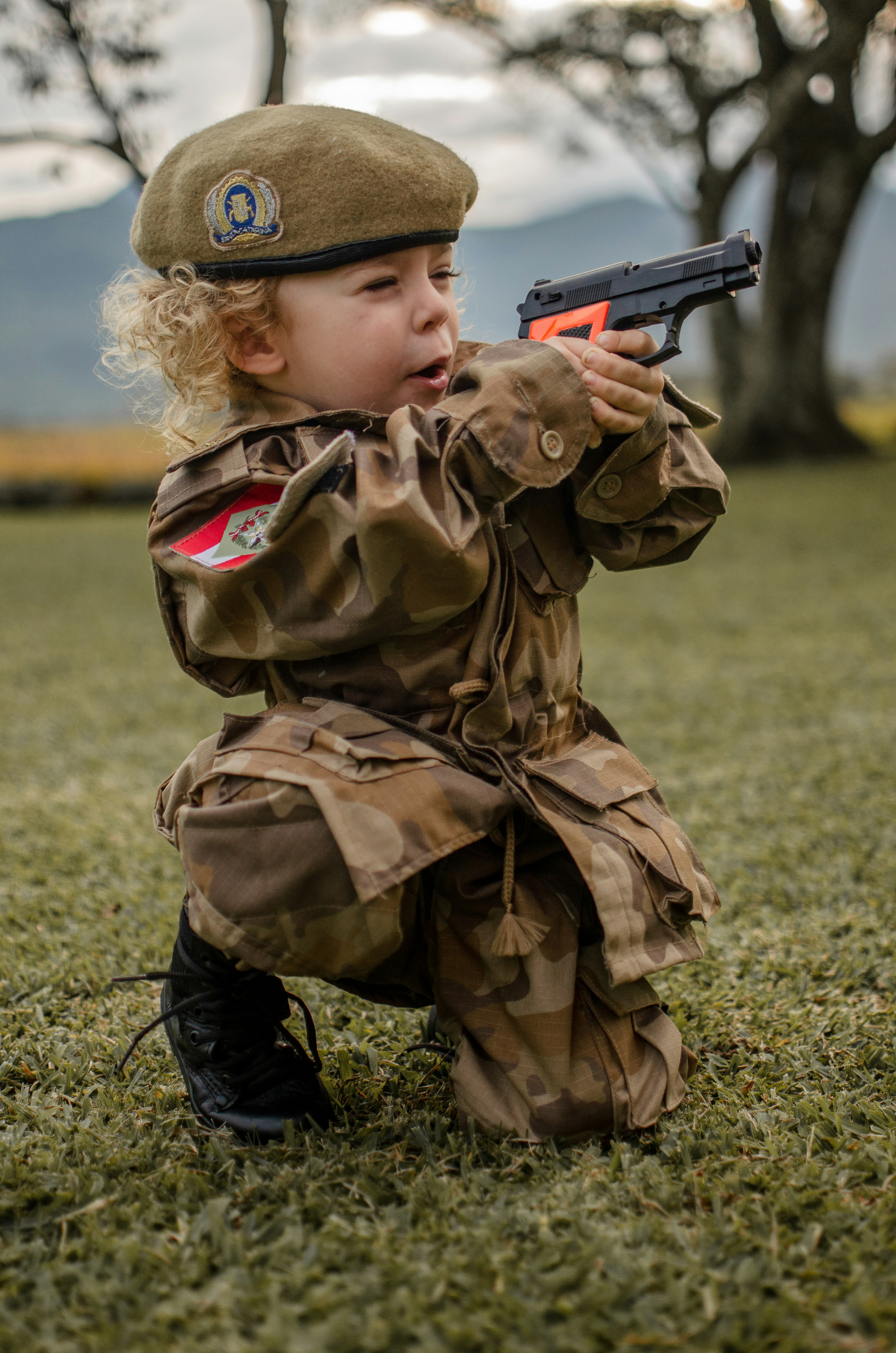 Niño con uniforme de camuflaje verde marrón sosteniendo un rifle negro