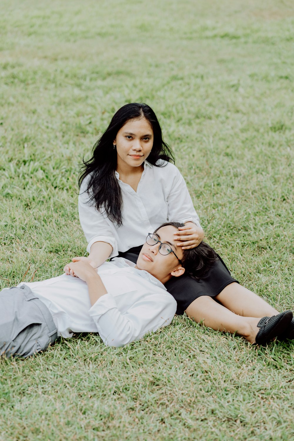 woman in white dress shirt and black skirt lying on green grass field during daytime