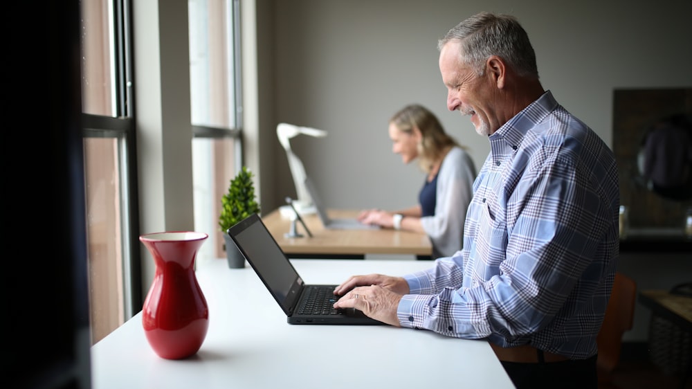 homem na camisa social xadrez azul e branco usando o computador portátil preto