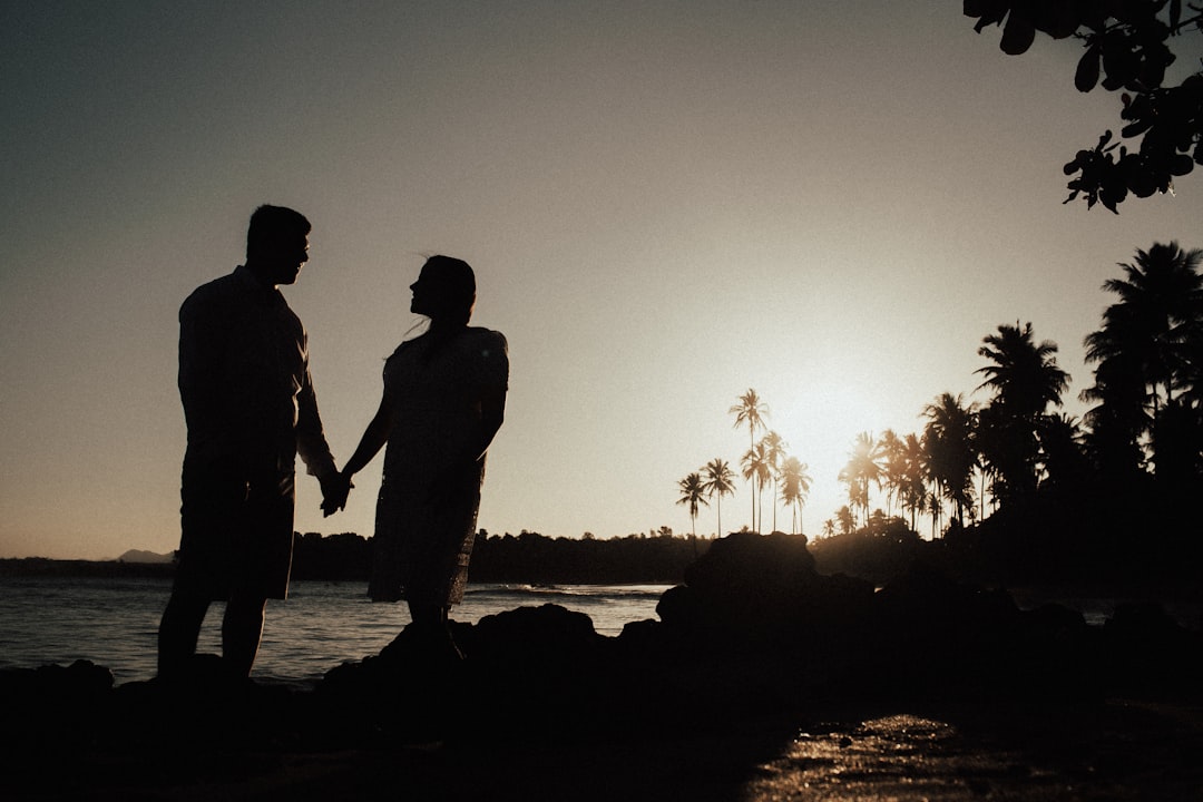 silhouette of couple standing on rock near body of water during sunset