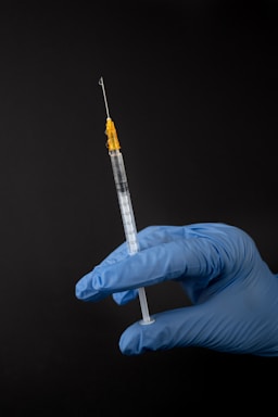 A close-up of a professional piercer's gloved hands holding a sterile piercing needle against a dark, elegant background.
